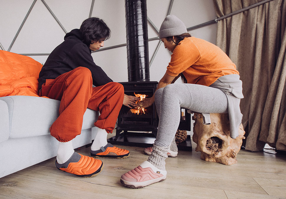 Two people warming their hands on a wood burning stove.