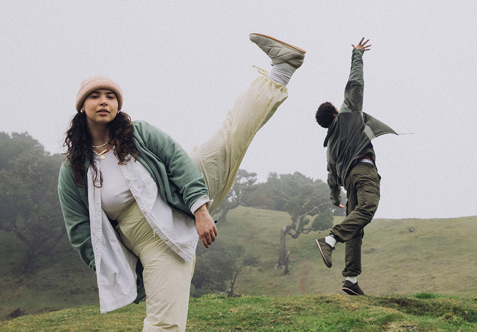 Two people, playing around in a grassy hill, wearing Teva 'ReEmber' shoes.