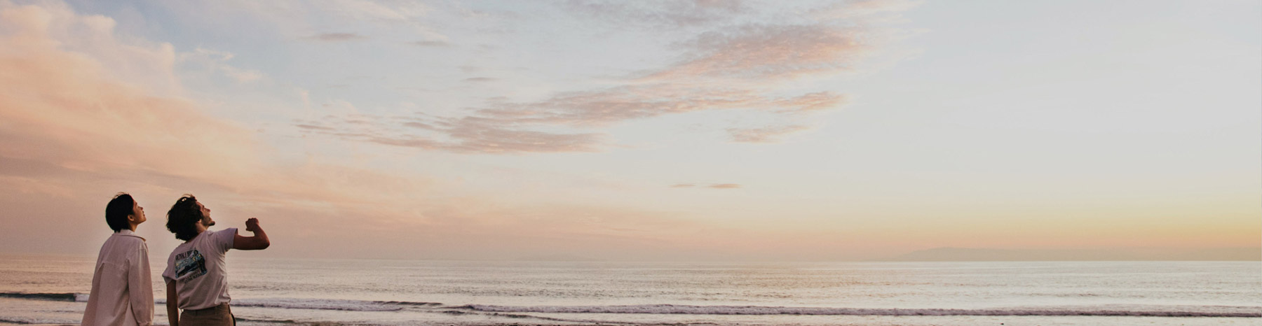 Couple standing by the beach, looking out at the sky.