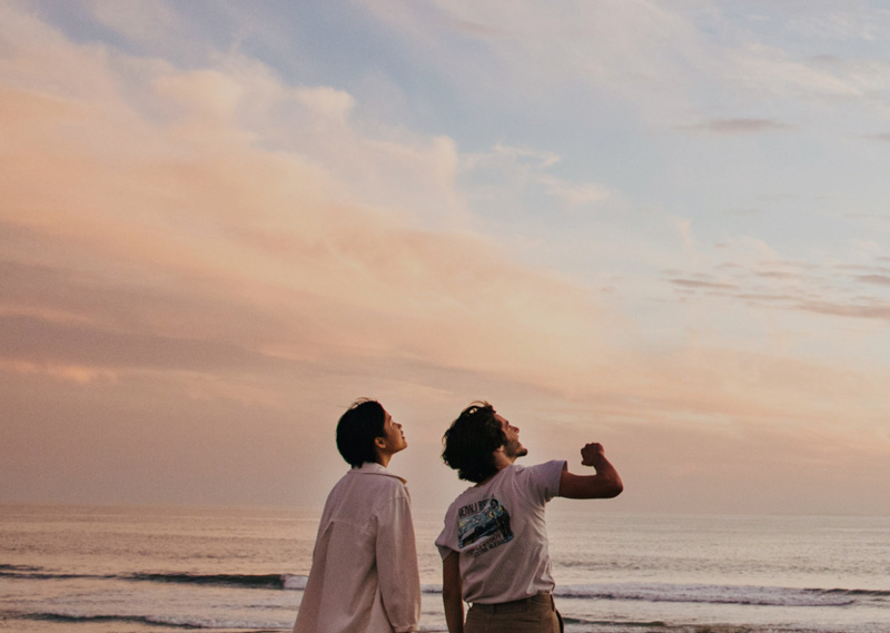 Couple standing by the beach, looking out at the sky.