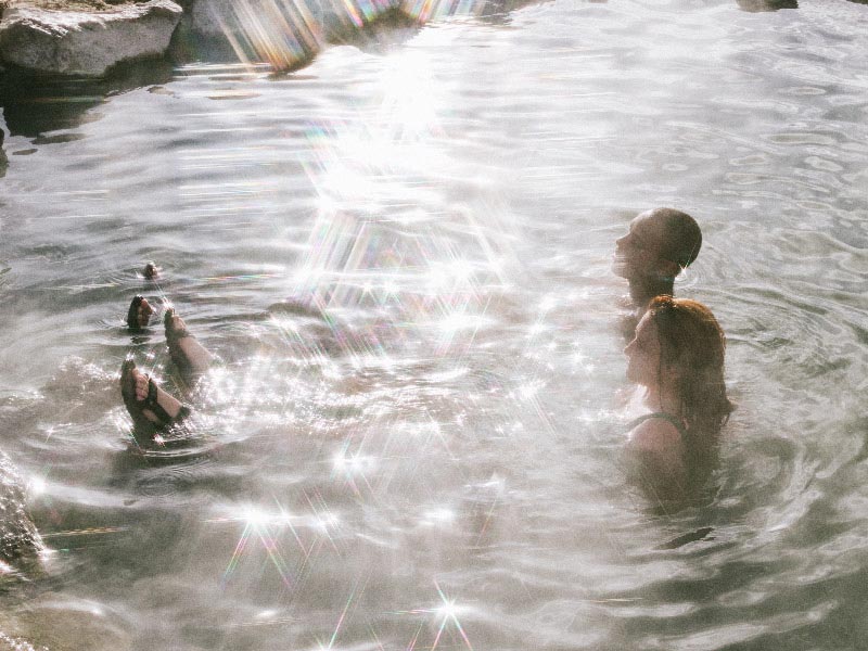 Couple swimming in water, with their feet showing out of the water - both wearing Tevas.