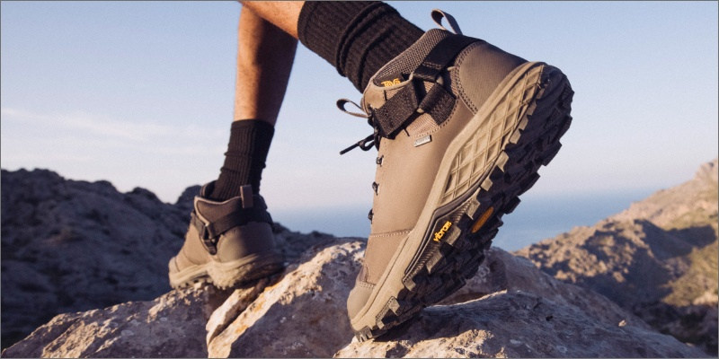Close up of a walking person's feet wearing Teva boots on rocky ground