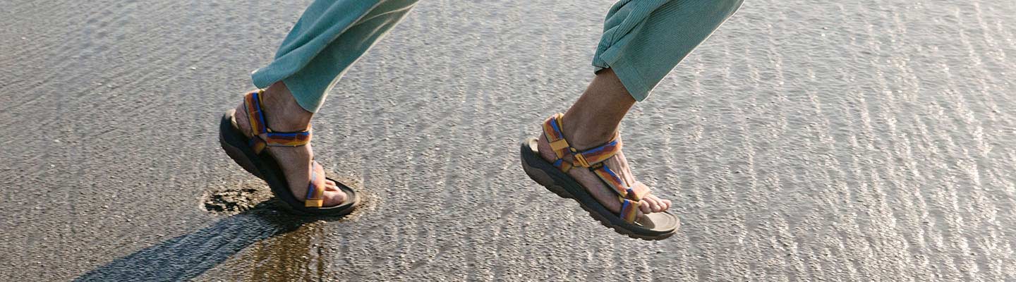Mens New Arrivals A man running on the beach wearing Teva Sandals.