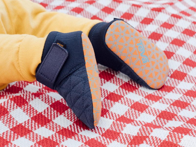 A kid laying on a blanket while wearing Teva shoes.