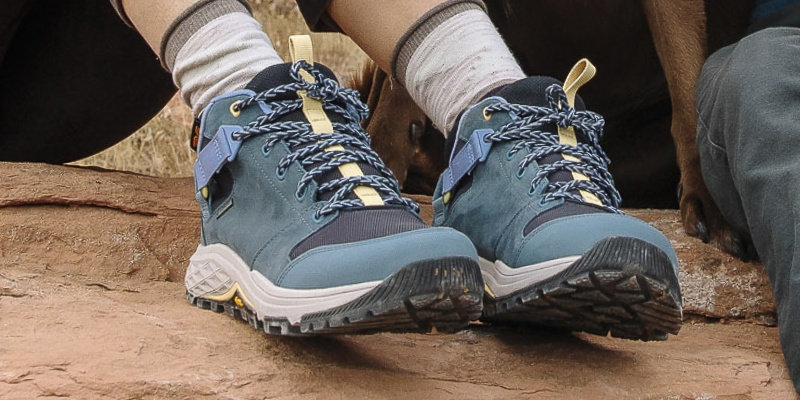 Close up of a person's feet wearing Teva boots on a rocky ground.