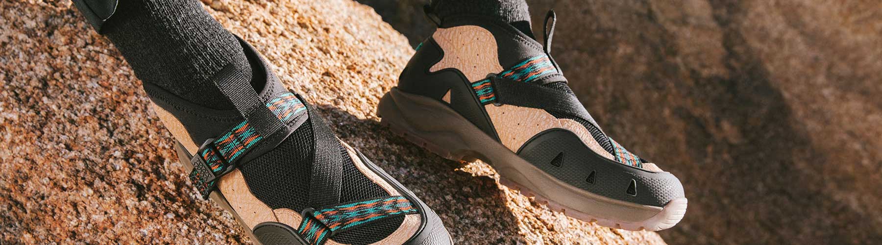 Close up of a man's feet wearing Teva shoes, with natural rock in the background.