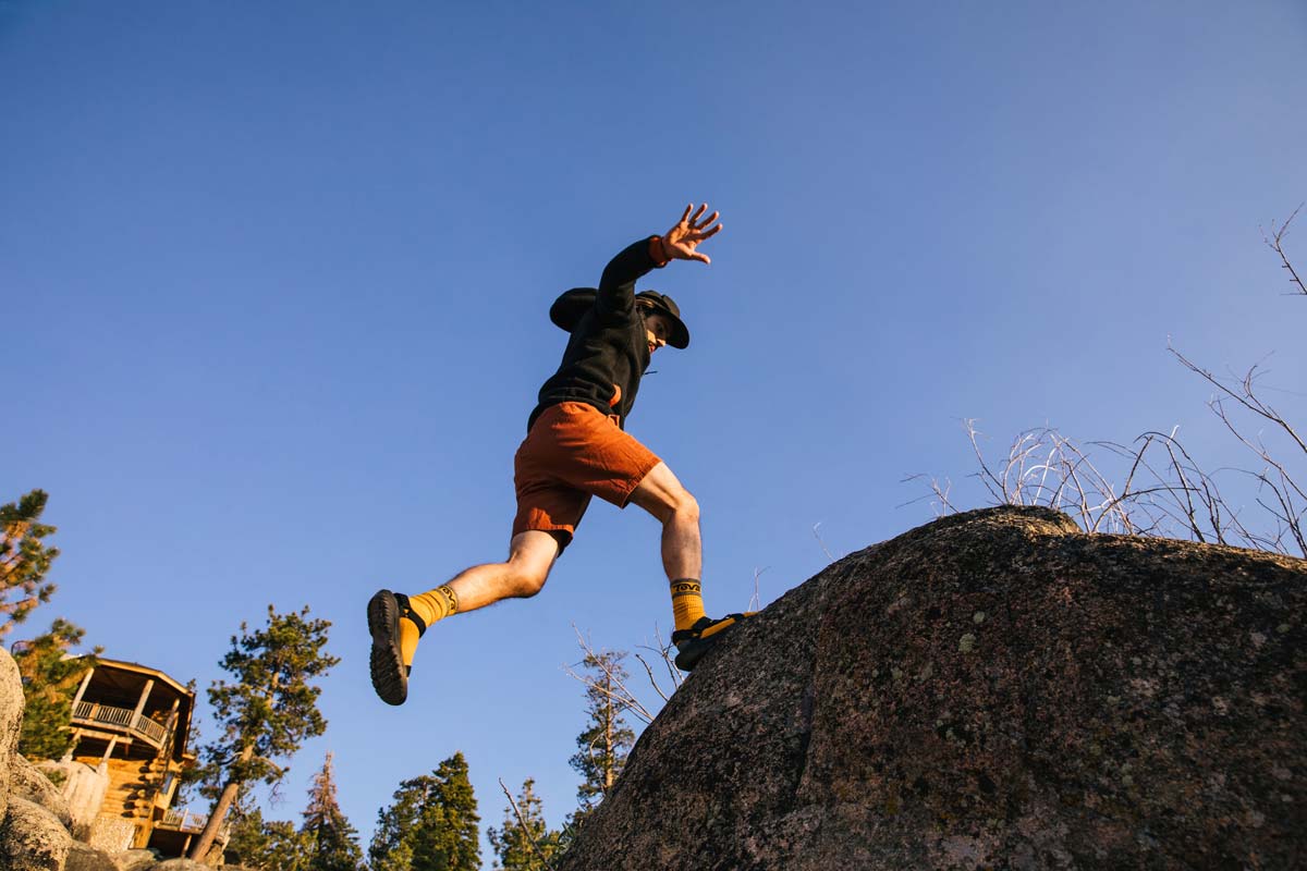 A man jumping on a rock with a house in the background.