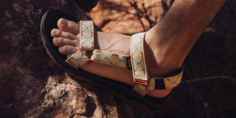 Close up of someone's foot, wearing Teva Sandals, walking on a rock.