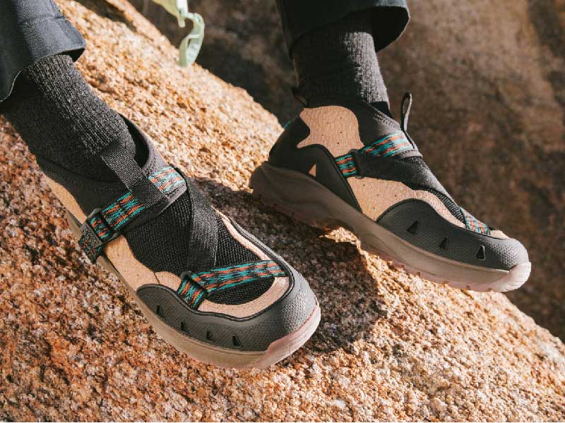 Close up of a man's feet wearing Teva shoes, with natural rock in the background.