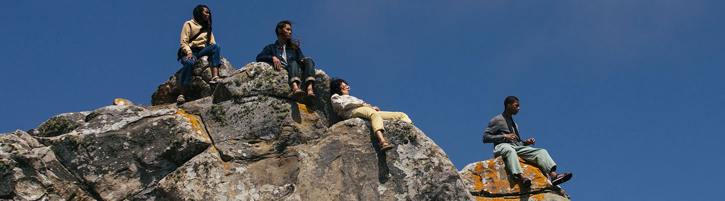 Group of people wearing Tevas, relaxing on the boulders of a mountain top.