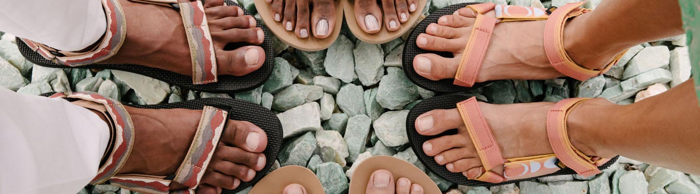 Close up of four people's feet, wearing Teva Sandals, standing on rocks.