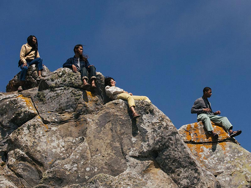 Group of people wearing Tevas, relaxing on the boulders of a mountain top.