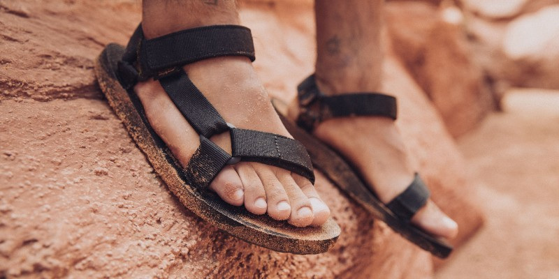 Close up of a person's feet walking on rocky ground while wearing Teva sandals.