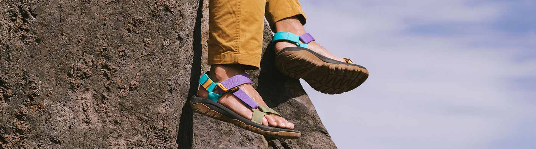 Mens Sandals Close up of a person wearing Teva Sandals sitting on a cliff.